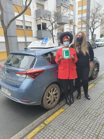 Dos personas con la placa L junto al coche de prácticas de Autoescuela Larimar