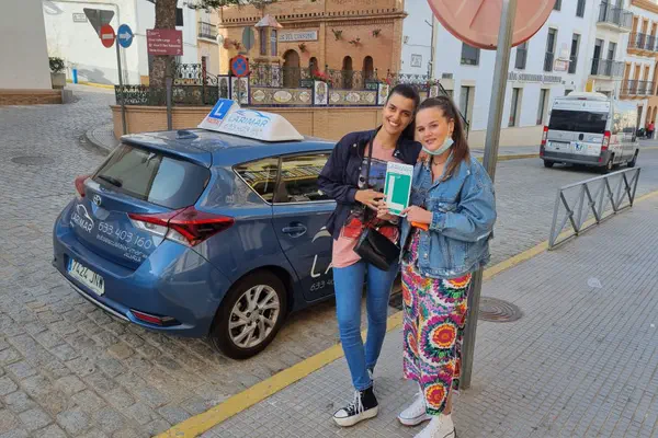 Dos personas con la placa L junto al coche de prácticas de Autoescuela Larimar