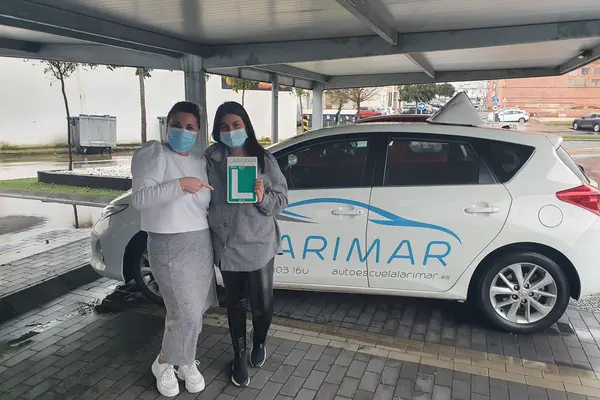 Dos personas con la placa L junto al coche de prácticas de Autoescuela Larimar