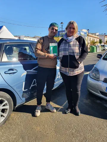 Dos personas con la placa L junto al coche de prácticas de Autoescuela Larimar