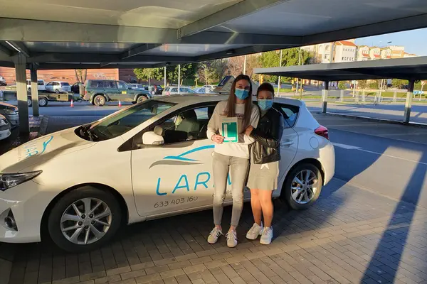 Dos personas con la placa L junto al coche de prácticas de Autoescuela Larimar