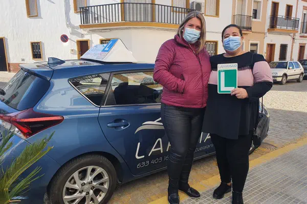 Dos personas con la placa L junto al coche de prácticas de Autoescuela Larimar