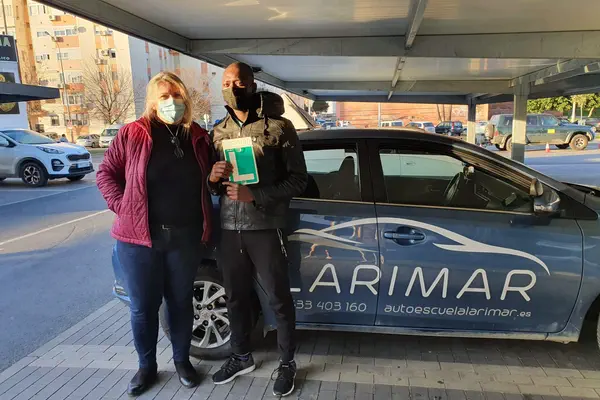 Dos personas con la placa L junto al coche de prácticas de Autoescuela Larimar