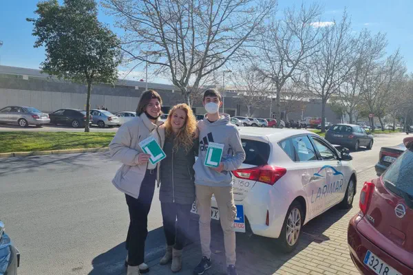 Tres personas con la placa L junto al coche de prácticas de Autoescuela Larimar