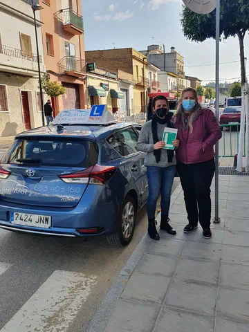 Dos personas con la placa L junto al coche de prácticas de Autoescuela Larimar